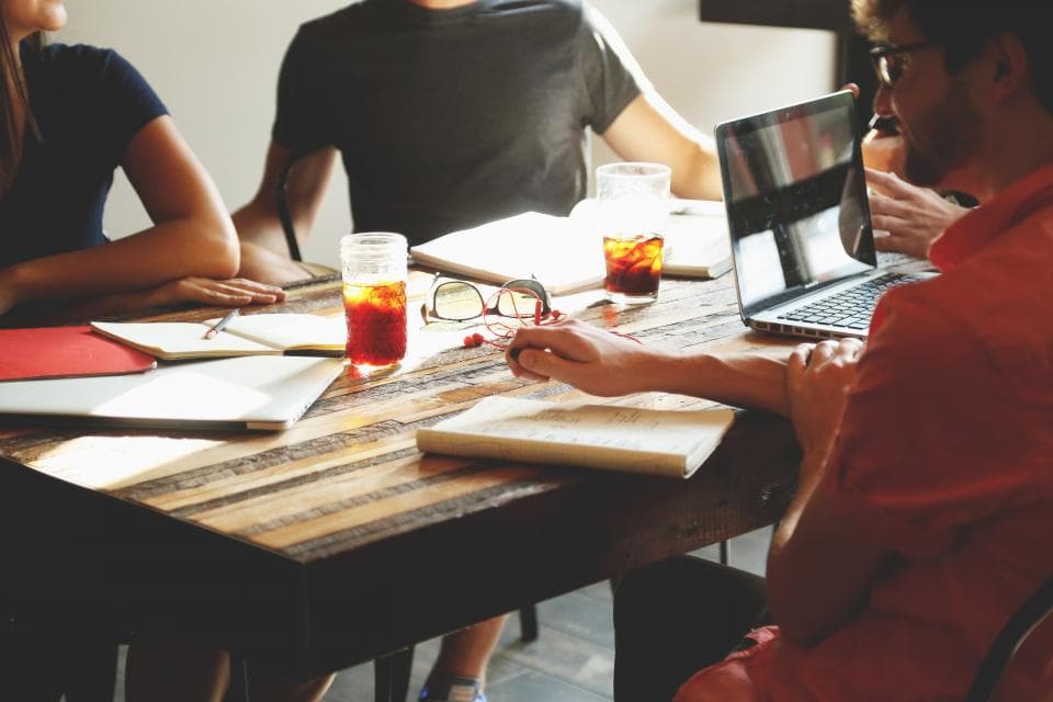 Colleagues sitting around a wooden table with notebooks, drinks and an open laptop during a team meeting
